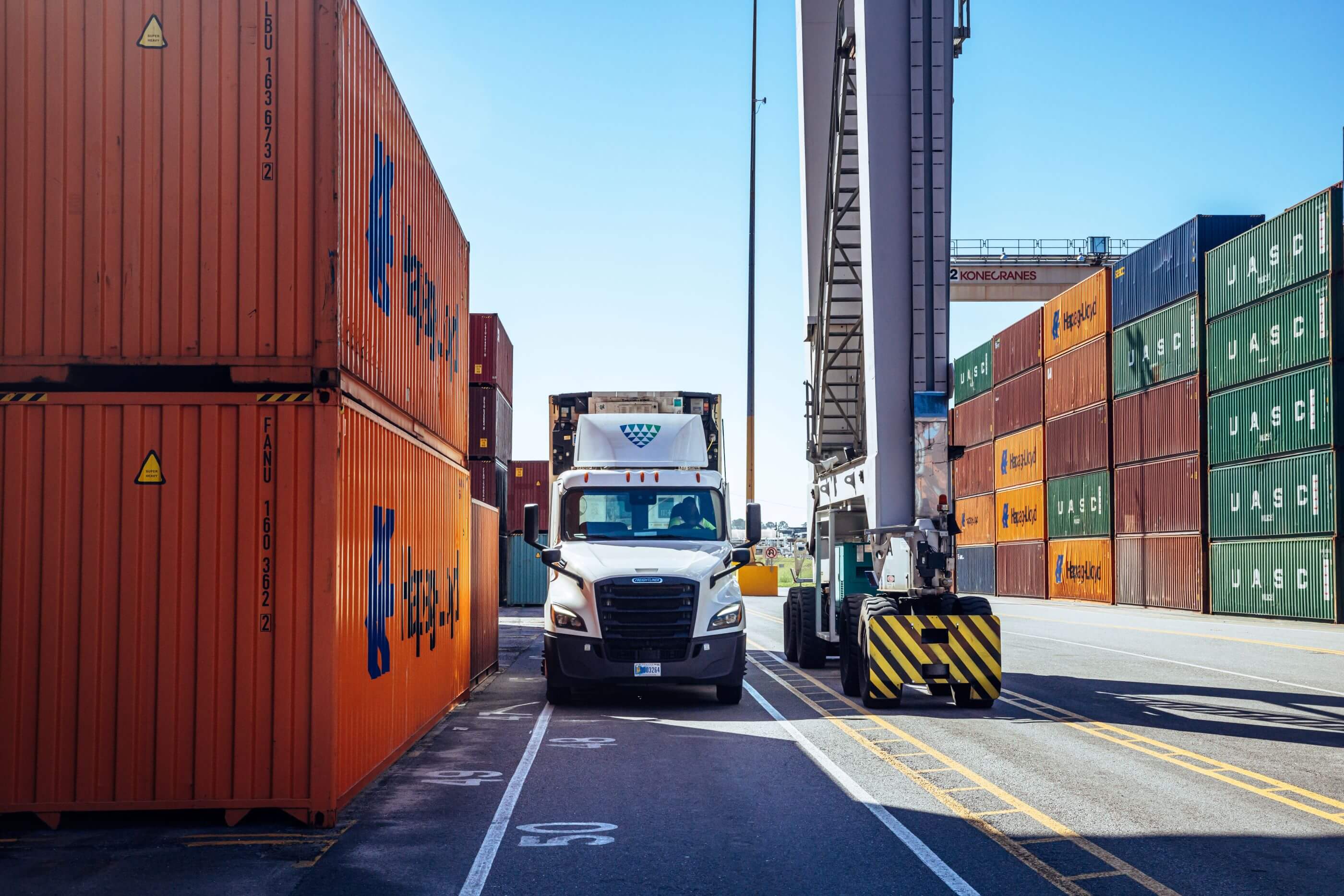 A Lineage artic-truck navigating between stacks of colourful shipping containers at a port.