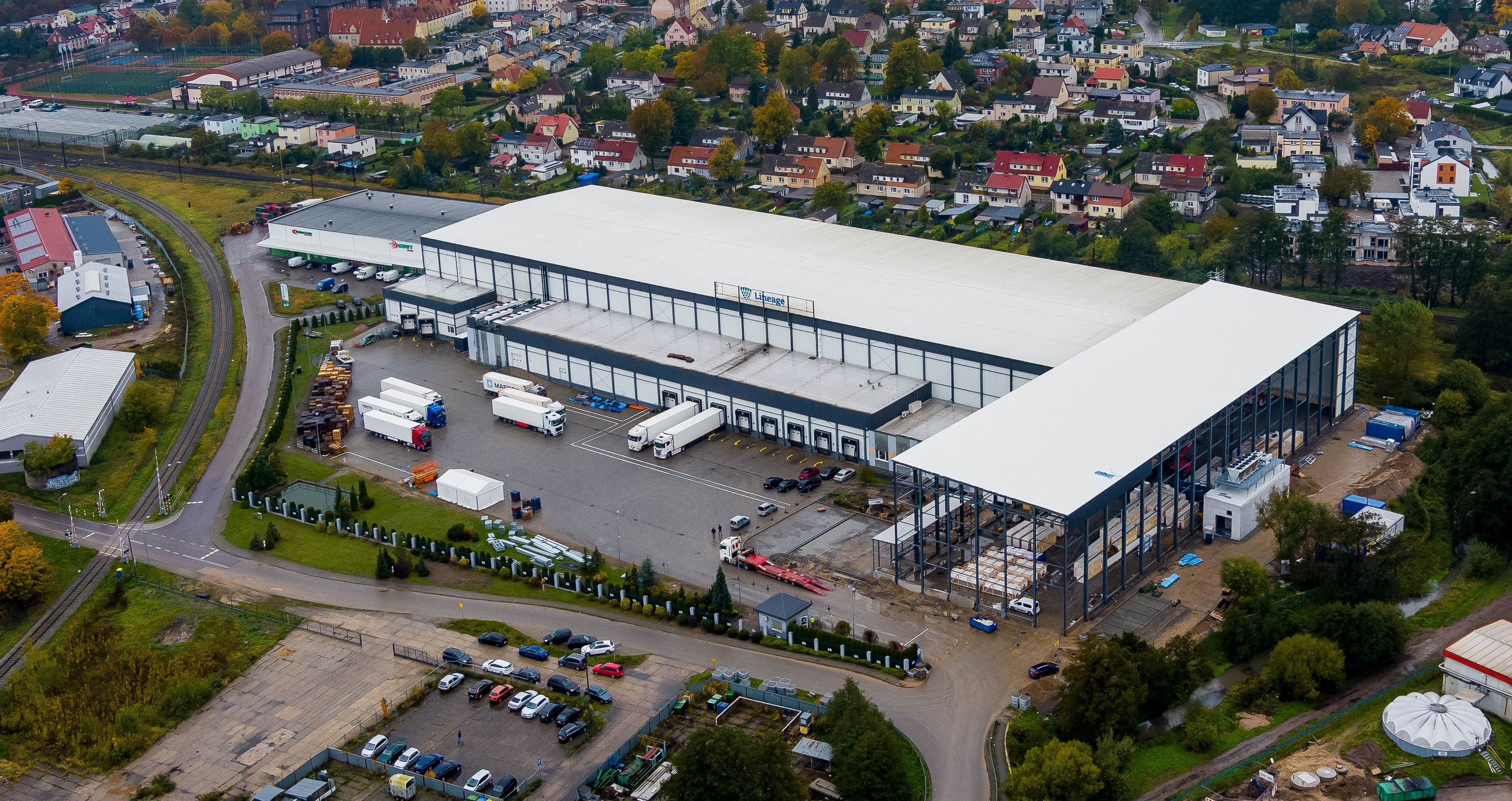 Widok z lotu ptaka na nowo rozbudowany magazyn Lineage z kontrolowaną temperaturą w Lęborku w Polsce pokazuje duży magazyn z kilkoma ciężarówkami zaparkowanymi w pobliżu.