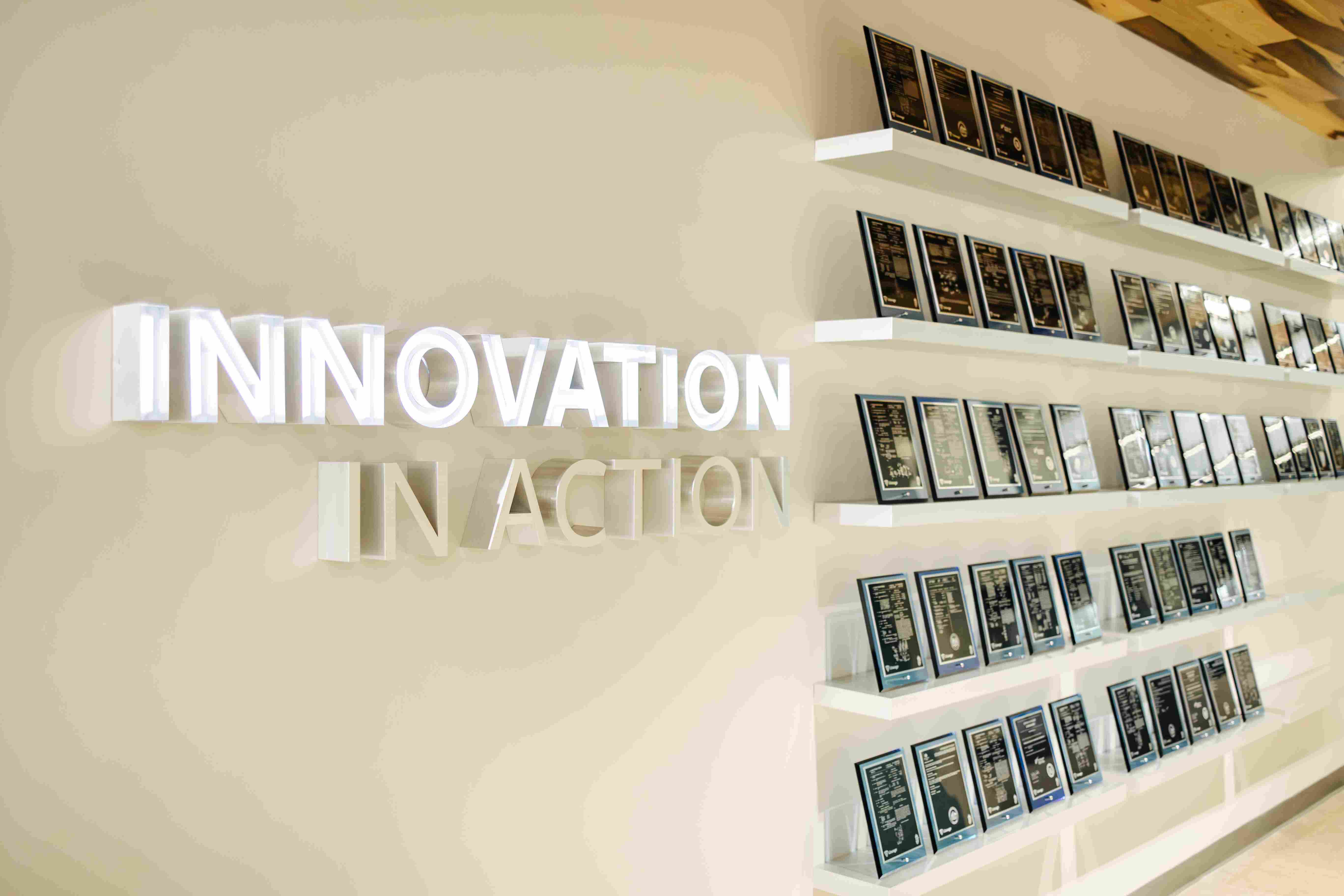 Na ścianie wewnątrz siedziby głównej Lineage w Novi widnieją tabliczki z patentami umieszczone na białych półkach obok trójwymiarowego znaku z napisem „Innovation In Action” (Innowacje w działaniu).