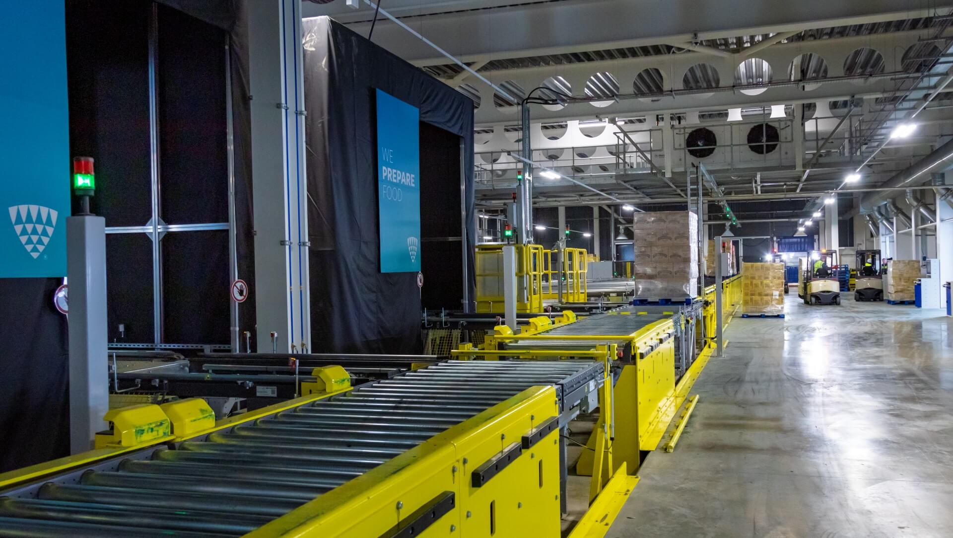 Nowoczesny magazyn chłodniczy z żółtymi systemami przenośników i wózkami widłowymi przenoszącymi palety. Automatyzacja Lineage Eye usprawnia odbiór i zarządzanie zapasami.