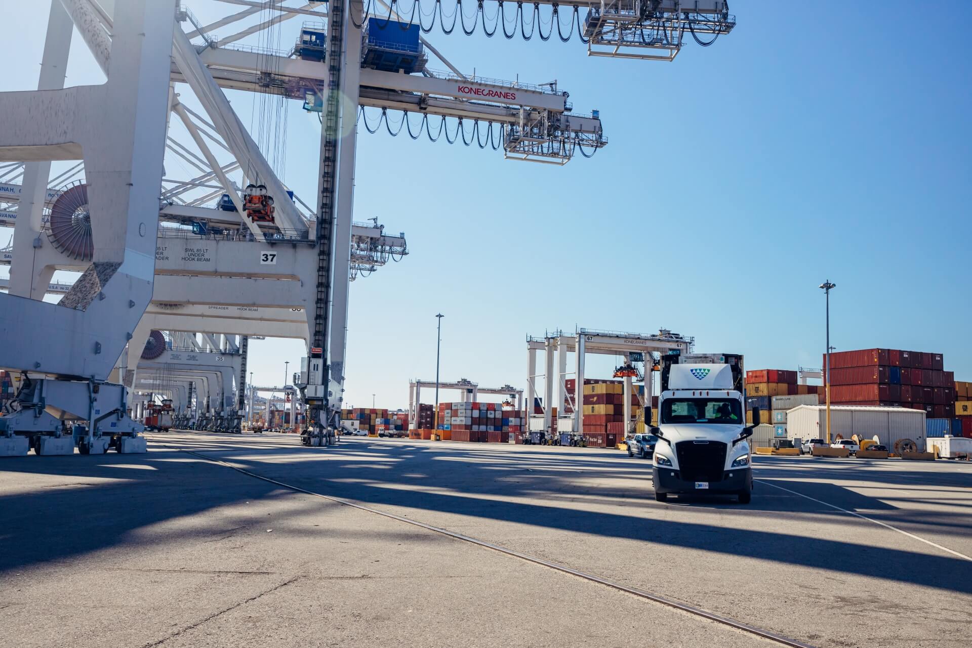 Lineage truck driving through a container port surrounded by cranes and stacked shipping containers, highlighting import/export and drayage operations