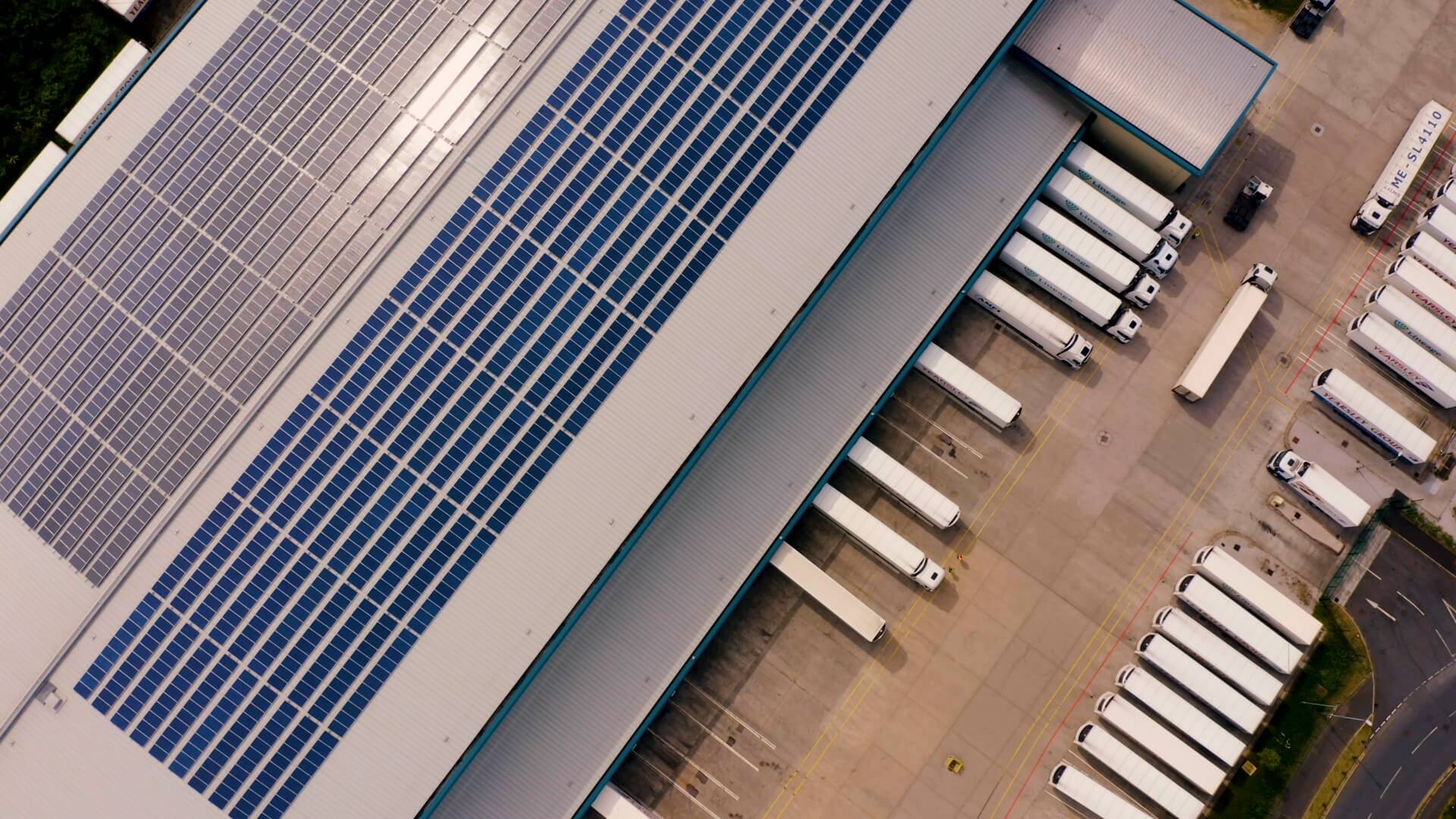 Widok z góry magazynu Lineage w Wielkiej Brytanii z panelami słonecznymi na dachu i ciężarówkami przy rampach załadunkowych.