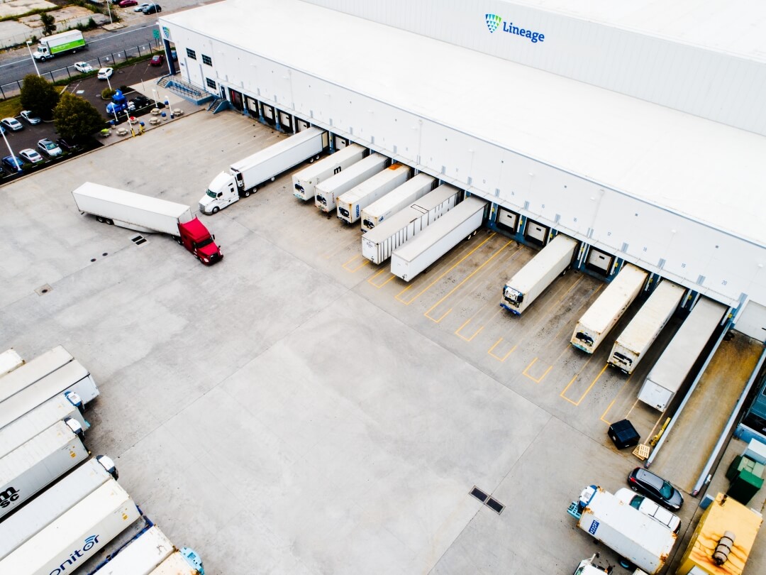 Aerial view of Lineage facility with refrigerated trucks loading and unloading at multiple docks, representing foodservice distribution and last-mile delivery operations.
