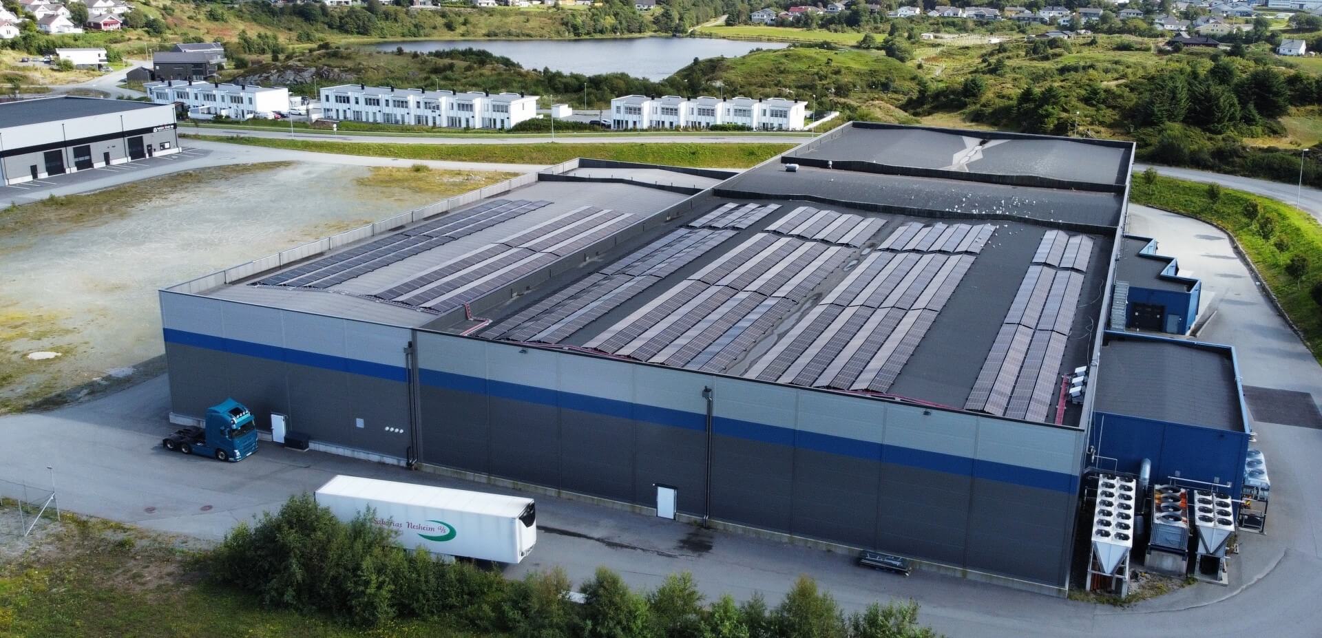 Luftaufnahme des Lineage in Haugesund, Norwegen, mit Solaranlage auf dem Dach, Ladezonen sowie der umliegenden Wohnbebauung und Naturlandschaft.