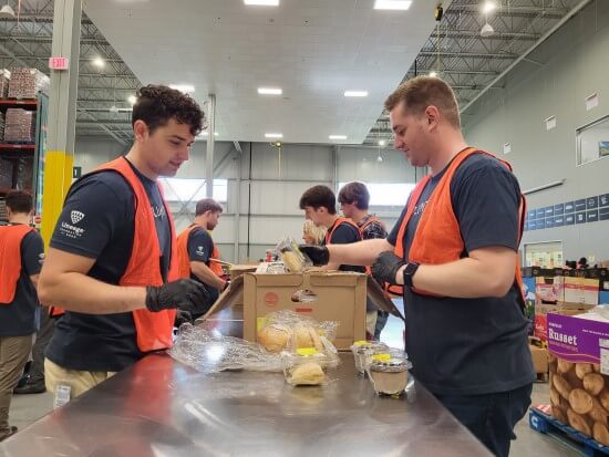 Lineage team members wearing orange vests and gloves packing food items into boxes at a food distribution center.