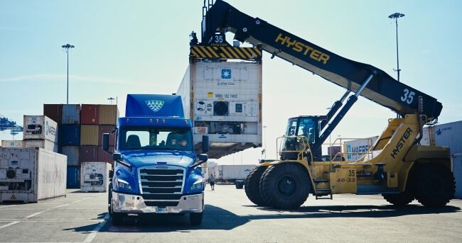 Lineage-branded truck at a port as a container is loaded by a Hyster forklift, showcasing drayage and port logistics operations