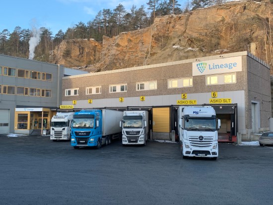 Lkw, die vor dem Lineage in Moss, Norwegen, geparkt sind; das Gebäude ist in einen felsigen Hang gebaut und dient als temperaturgeregeltes Lager mit mehreren Laderampen.