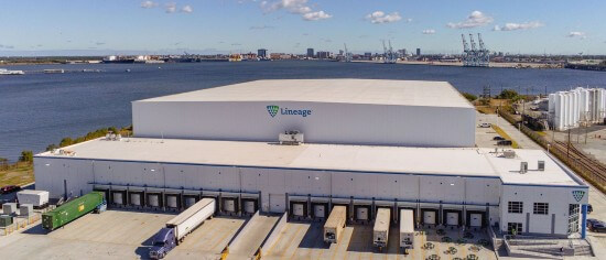 A Lineage port-centric cold storage warehouse sits along the waterfront with trucks at the dock doors and cranes visible across the bay, highlighting fast access between port operations and temperature-controlled storage.