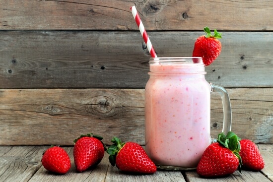 Strawberry smoothie served in a glass jar with a striped straw, surrounded by fresh strawberries, representing nutritious meals provided through Lineage's donation partnerships.