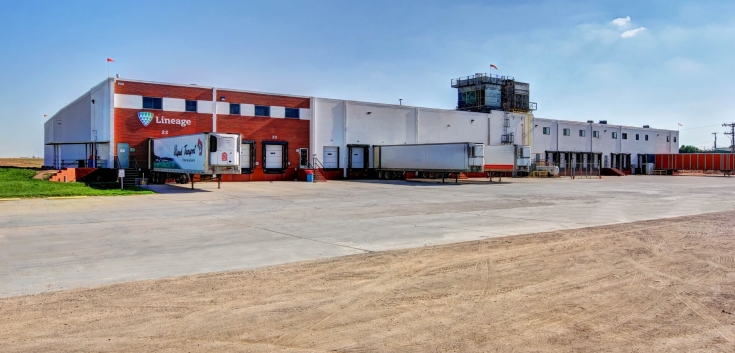 Exterior view of the Lineage cold storage facility in Friona, Texas, with the brick-and-white warehouse, loading docks and trailers under a clear sky.