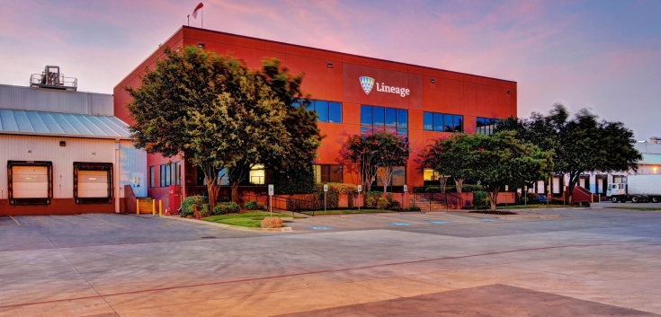 Exterior of the Lineage facility in Fort Worth, Texas, with the red office building, loading docks and surrounding trees at dusk.