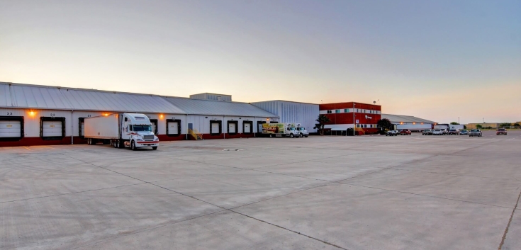 Wide view of Lineage’s McAllen South Ware facility, showing the loading docks, trucks and the red office building at dusk.