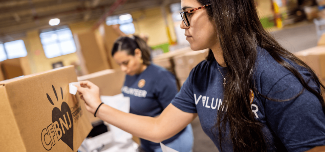 Two Lineage volunteers, wearing blue "Volunteer" shirts, pack and label boxes of food inside a warehouse, preparing food for donation to food insecure communities.
