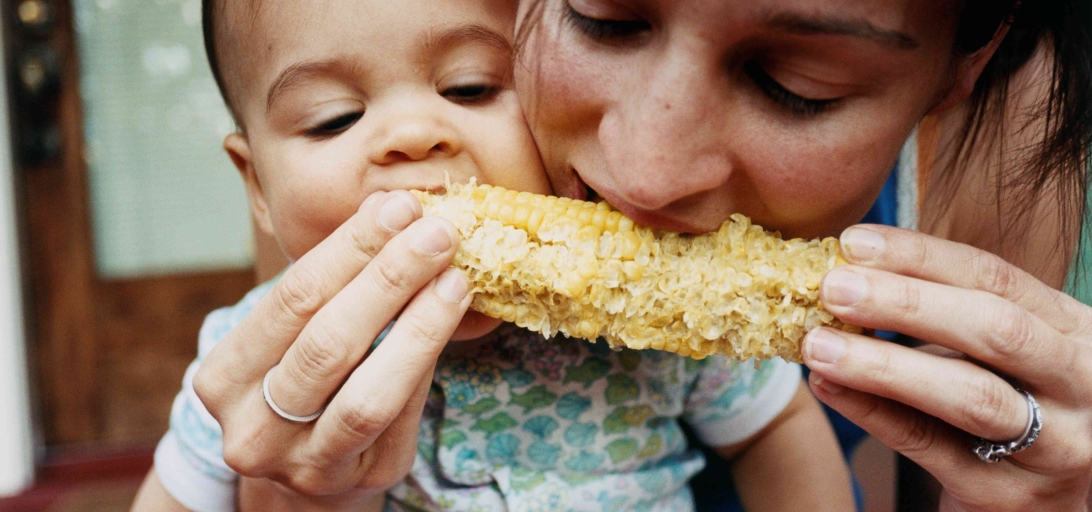 A mother and young child share corn on the cob