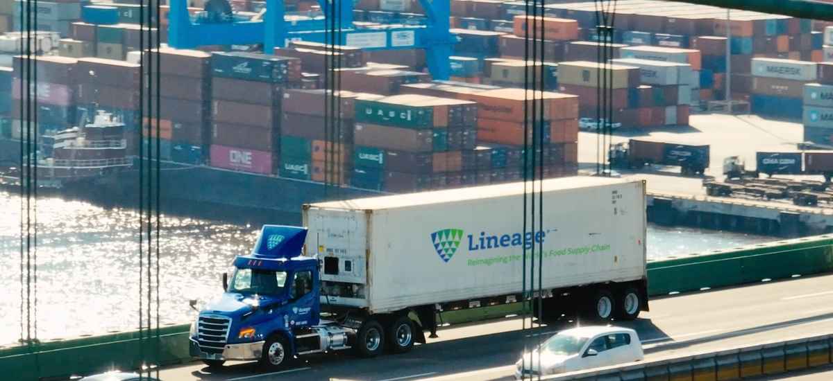 A Lineage truck crossing a bridge with a port full of shipping containers in the background, representing supply chain solutions for navigating tariffs and global trade challenges.