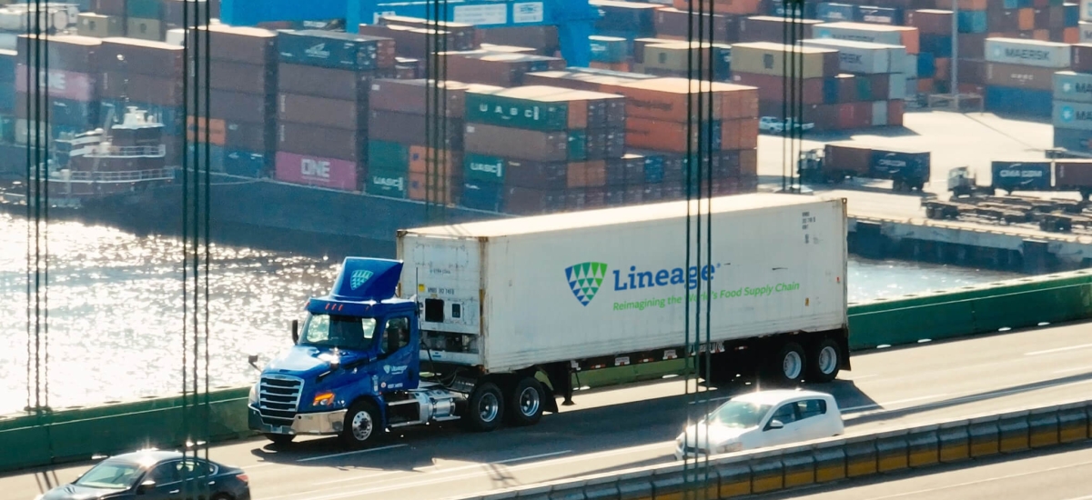 A Lineage truck crossing a bridge with a port full of shipping containers in the background, representing supply chain solutions for navigating tariffs and global trade challenges.
