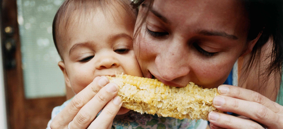 A mother and young child share corn on the cob