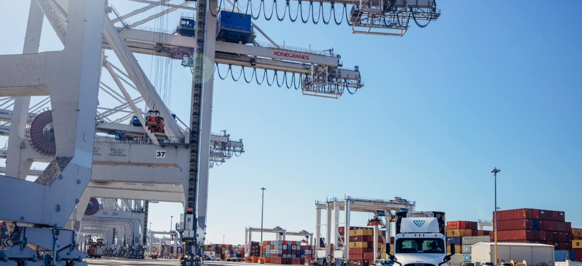 Lineage truck driving through a container port surrounded by cranes and stacked shipping containers, highlighting import/export and drayage operations