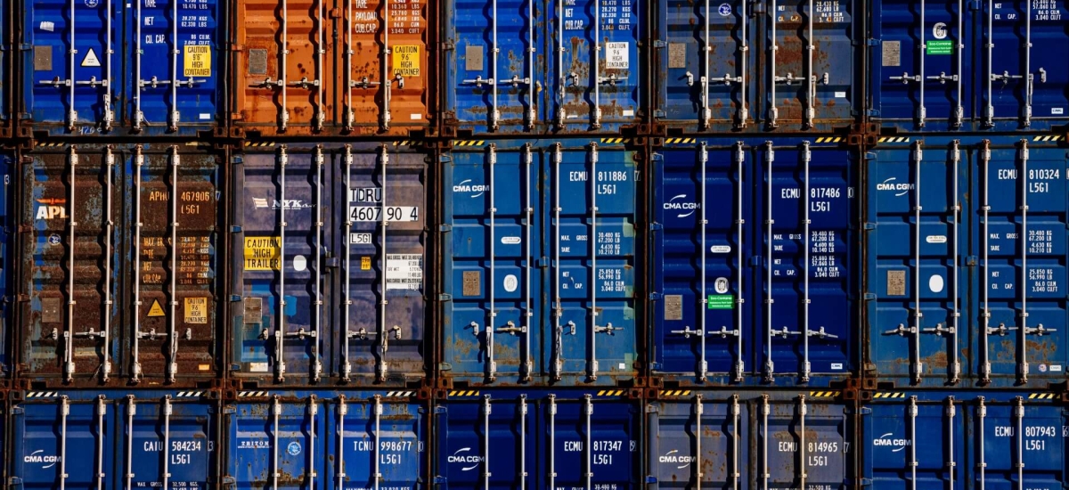 Stacked shipping containers at a busy port terminal, representing U.S. food exports, global trade logistics and temperature-controlled ocean freight movement.