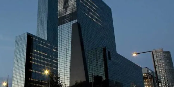 Skyscraper complex with reflective glass facade at dusk, city streetlights and buildings nearby