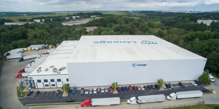 Aerial view of Lineage's College Park cold storage facility in Atlanta, GA, featuring a large warehouse, multiple truck bays, parked trailers, and surrounding green landscape, highlighting advanced logistics infrastructure.