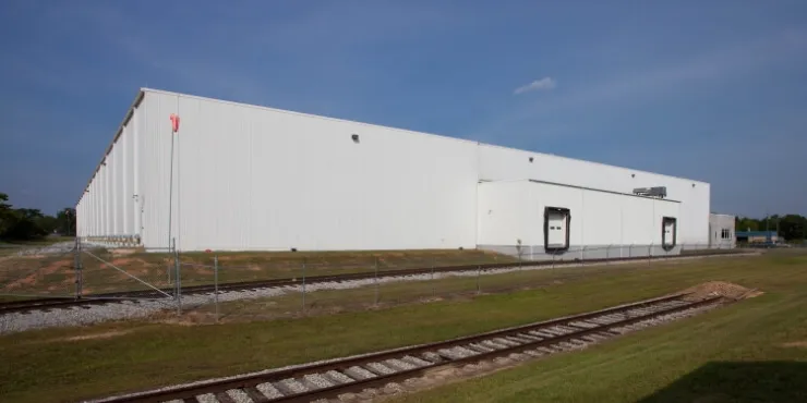 Exterior side view of Lineage’s Macon cold storage facility in Atlanta, Georgia, featuring a white warehouse, adjacent rail tracks, and a grassy foreground.