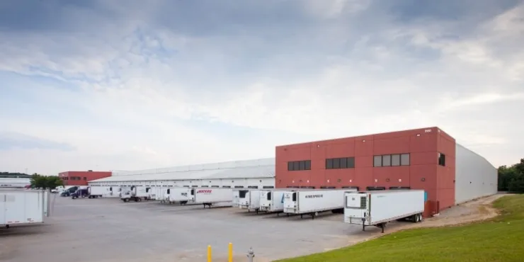 Side view of Lineage’s McDonough -  200 King Mill cold storage facility, showcasing docked refrigerated trailers, a red-brick structure, and open loading areas.