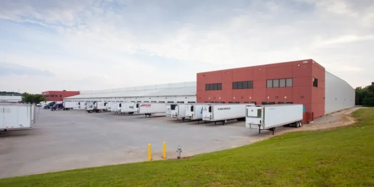Side view of Lineage’s McDonough -  200 King Mill cold storage facility, showcasing docked refrigerated trailers, a red-brick structure, and open loading areas.