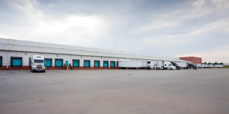 Dockside view of Lineage’s McDonough -  200 King Mill cold storage facility, featuring multiple loading bays, semi-trailers, and a spacious concrete yard.