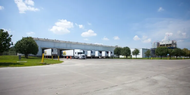 Side view of Lineage’s Unadilla cold storage facility near Atlanta, Georgia, showcasing docked refrigerated trailers, surrounding greenery, and open parking areas under a clear blue sky.