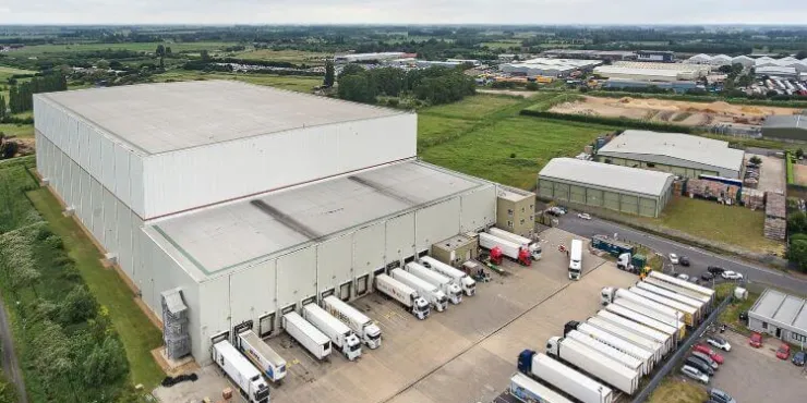 Ampia ripresa aerea del centro di stoccaggio frigorifero Lineagea Wisbech – Boleness, circondato da terreni agricoli e stabilimenti industriali, con i rimorchi in fila davanti alle banchine.