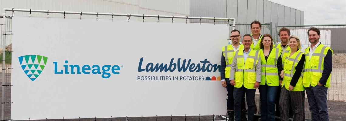 A group of people in high visibility gear stand near a sign announcing Lineage's expansion with customer Lamb Weston
