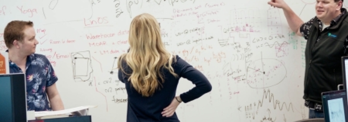 Lineage team members collaborating in an office, reviewing and discussing supply chain concepts and data sketched across a whiteboard during a working session.
