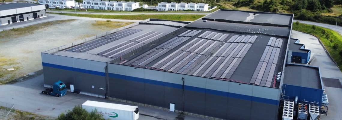 Vista aerea del centro di stoccaggio Lineage a Haugesund, in Norvegia, con pannelli solari sul tetto, aree di carico e il paesaggio residenziale e naturale circostante.