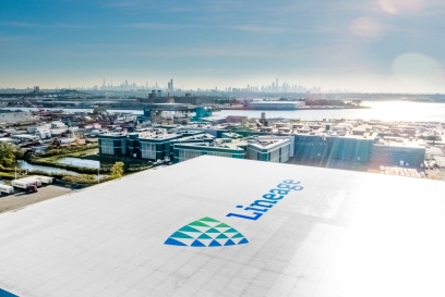 Aerial view of a Lineage cold storage facility near a major port, with the city skyline in the background