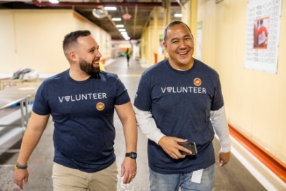 Two Lineage team members wearing “Volunteer” shirts walk together through a warehouse facility, smiling during a community volunteer event.