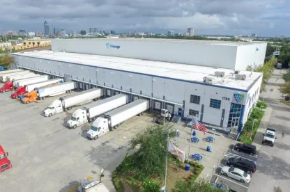 Exterior shot of Lineage's West Beaver cold storage warehouse in Jacksonville with multiple trucks at the loading bays, under a cloudy sky. 