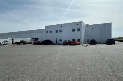 Exterior view of Lineage's Pasco cold storage warehouse in Washington, featuring a modern white facility with parked trucks, cars, and spacious lot for logistics operations.