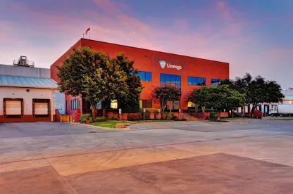 Exterior of the Lineage facility in Fort Worth, Texas, with the red office building, loading docks and surrounding trees at dusk.