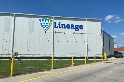 Exterior view of Lineage’s Houston Hwy 225 facility, showing the white warehouse wall with the Lineage logo, yellow safety bollards and a clear blue sky.