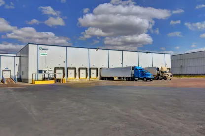 Esterno della struttura militare Lineagea McAllen West, con il magazzino bianco dotato di diverse banchine di carico e numerosi camion parcheggiati sotto un cielo parzialmente nuvoloso.