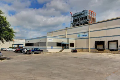 Exterior view of Lineage’s San Antonio Profit facility, showing the light-colored warehouse, loading docks and parked vehicles under a partly cloudy sky.